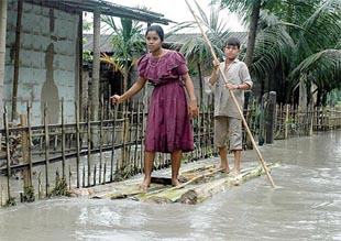 A girl with her brother travels on a makeshift raft in front of their house 