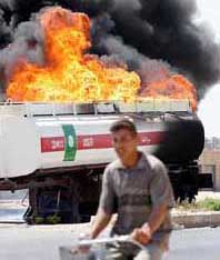 An Iraqi youth rides his bicycle past a burning oil tanker 