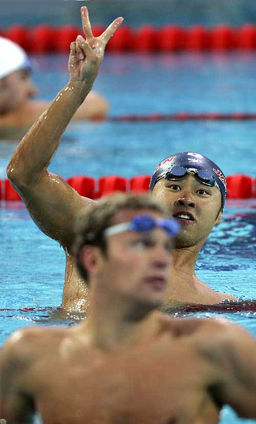 Japan's Kosuke Kitajima flashes a victory sign behind Brendan Hansen of the U.S after winning the men's 100 metres breaststroke final at the Athens 2004 Olympic Games August 15, 2004. Kosuke took the gold medal in a time of one minute 00.08 second while Hansen finished second. REUTERS/Jerry Lampen