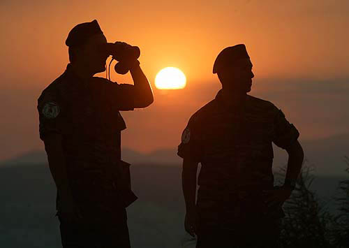Greek soldiers stand on a hilltop overlooking the Athens Olympic Stadium at sunset August 29, 2004, prior to the closing ceremony of the Athens 2004 Olympic Games. REUTERS/Jason Reed