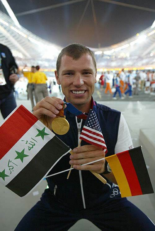 Jason Read of the U.S., who won a gold medal in the men's eight rowing, holds an Iraqi flag (L), a German flag (R) and a U.S. flag during the closing ceremony of the Athens 2004 Olympic Games August 29, 2004. The next summer Olympic Games will be held in Beijing in 2008. REUTERS/Kimimasa Mayama