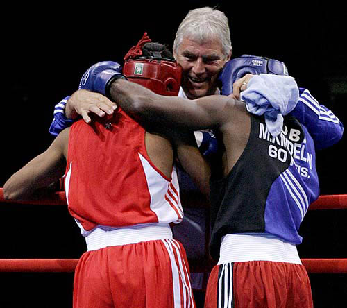 Coach of Britain's Amir Khan, Terry Edwards (centre) hugs him and Cuba's Mario Cesar Kindelan Mesa (right) after the lightweight (60kg) finals bout at the Athens 2004 Olympic Games on August 29. Cuba's Mario Cesar Kindelan Mesa won the fight.