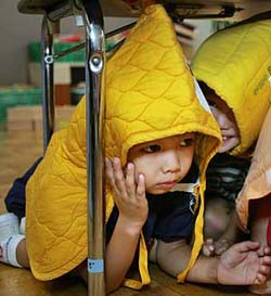 A four-year-old Japanese boy in a padded protective hood takes cover under a table during an earthquake drill in Tokyo 