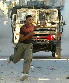 A Palestinian youth runs in front of an Israeli jeep