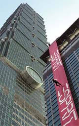 A model climbs down the side of a shopping mall against the backdrop of the Taipei 101 building