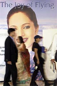 People walk past a billboard advertising an airline company during the travel and tourism fair organised by the Travel Agents Association of India, in Kolkata