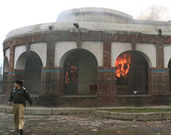 A police officer walks in front of the burning office of the Mayor, set on fire by angry Shiites mourners, in Sialkot, 230 km southeast of Islamabad, on Saturday