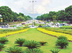 Dense clouds hover over the city, traffic flows on road dotted with trees on sides and Shivaliks in the backdrop 