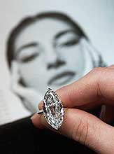 An employee of Sotheby's displays a 11.7-carat marquise-shaped diamond ring beneath a portrait of the opera legend Maria Callas during a press preview at Sothebys in Geneva on Monday