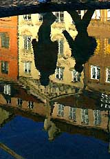 Two boys are reflected on the water of a fountain as they walk through the old town of Warsaw 