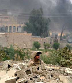 A US Marine of the Ist Marine Division conducts a search operation while columns of smoke rises after engagements in the war-torn city of Falluja on Tuesday