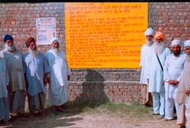 Residents of Kamalpur village in Samana subdivision stand next to the wall on which new panchayat laws have been painted.