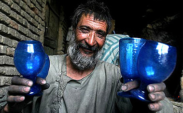 Afghan glass blower Sayedullah smiles as he poses, holding his handmade glasses at his workshop in Kabul on Sunday