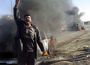 A man cheers next to burning pick-up trucks