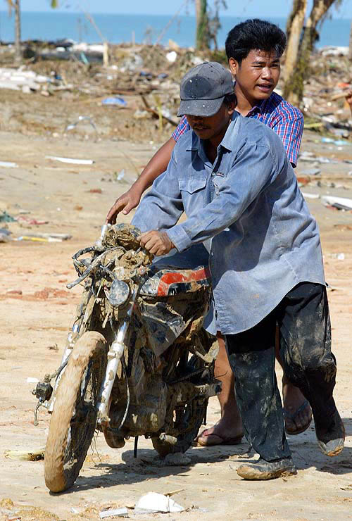 People push a motor cycle in Phang Nga province, about 788 km south of Bangkok on December 28, after a tsunami hit the area on Sunday.  Reuters