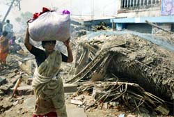 A tsunami survivor carries her belongings after her damaged house caught fire from flames of a funeral pyre in Nagapattinam port, 350 km from Chennai, on Wednesday. 
