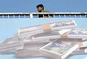 A Pakistani youth walks over a bridge upon which a billboard shows Pakistani currency in Rawalpindi