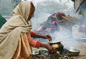 A woman cooks food on the roadside while her children hide under a blanket to ward off cold in Ludhiana
