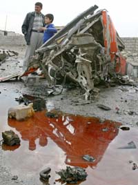 An Iraqi father and his son stand near the wreckage of a car bomb after it exploded as a US military convoy of Humvee vehicles was driving past in the northern city of Mosul