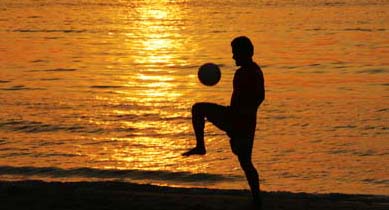 A Thai man plays football at sunset on Patong beach
