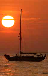The sun sets behind a boat at Kata beach in Phuket, Thailand, on Sunday