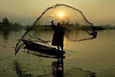 A fisherman casts his net as the sun sets over the Dal Lake in Srinagar on Monday