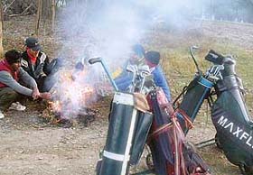 Caddies at the Chandigarh Golf Club sit around a fire to keep warm while golfing takes a backseat