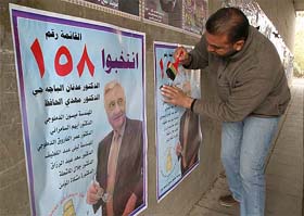 An Iraqi campaign worker hangs election posters of Adnan Pachachi