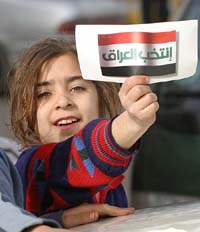 An Iraqi girl holds up a sign bearing her country's flag with Arabic writing in it