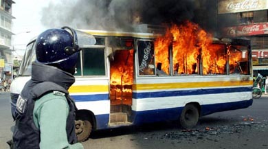 A Bangladeshi armed policeman looks on as an empty bus burns in Dhaka