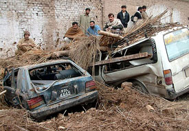Pakistani residents climb on to damaged cars after a roof collapsed following torrential rains in Peshawar on Saturday