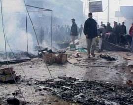 A video image shows Iraqis standing in debris and rising smoke on Monday following a suicide car bomb attack on a crowd of people in the town of Hilla, south of Baghdad, which killed 110 persons and wounded 130.   