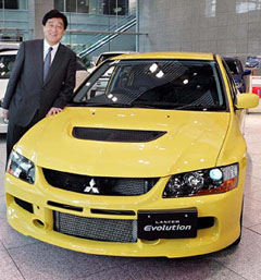 New President and Chief Operating Officer Osamu Masuko of Mitsubishi Motors Corp. poses with the automakers new Lancer Evolution at its showroom in Tokyo on Wednesday. Masuko said earlier in the day that the scandal-plagued Japanese automaker has no plans to sell its plant in the United States or further trim its work force there and remains committed to the US market, which is critical for the companys turnaround.