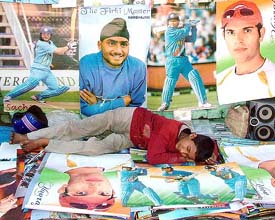 A street vendor displaying posters of popular Indian cricketers takes a nap on a Jammu road as people watch the first cricket test match between India and Pakistan on television, on Saturday afternoon