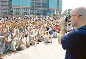 Ramon, a tourist from Switzerland, takes a photograph of the protest rally by the Kisan Hit Bachao Committee members at the PUDA office in Mohali