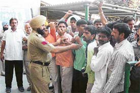 A policeman tries to stop activists of the Fruit and Vegetable Commission Agents Association and Rehri Union protesting against the auction of contract for the collection of market fee at the grain market in Mandi Ahmedgarh