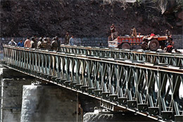 An Indian Army officer looks at the bridge at Kaman post near the LOC as locals from occupied Kashmir work on the Srinagar-Muzaffarabad Road.