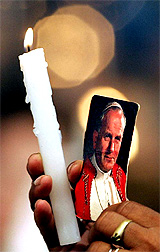 A worshipper holds a candle and an image of Pope John Paul II during a special mass at a church in Sao Paulo, Brazil, on Saturday