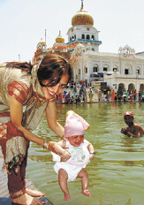 A young mother giving a dip to her newborn baby on the occasion of Baisakhi at Bangla Sahib Gurdwara in the Capital.