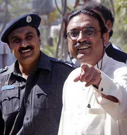 Asif Ali Zardari, husband of Benazir Bhutto, is escorted by a Pakistani policeman outside his residence in Lahore on Saturday