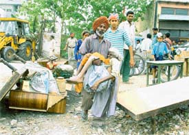 An alleged encroacher carries his elderly mother to a safer place as the demolition squad razed his house in Ludhiana on Friday