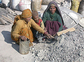 Bimla and Kanta pick out metal scrap from waste with the help of a magnet and the baby looks on.