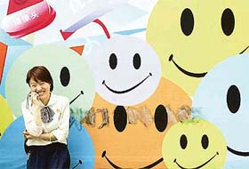 A Chinese saleswoman enjoys a chat on her mobile phone while standing against a billboard showing smileys in Chinas southwestern city of Chongqing