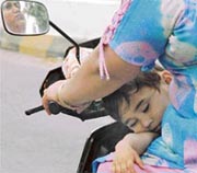 A child gets a nap on the lap of his mother who is driving a scooter on a hot afternoon