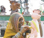 A roadside artist painting a smile on a clay figure. Quite pleased, she is unmindful of blistering sun