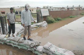 Children cross a flooded street through a temporary bandh constructed by residents with the help of gunny bags in the High Land Housing Society in Bartana near Zirakpur on Tuesday