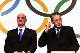 International Olympic Committee  President Jacques Rogge (right) removes a translation earpiece as senior IOC member Kevan Gosper looks on at a press conference after the conclusion of the 117th IOC session in Singapore 