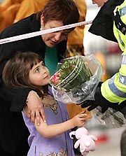 A girl gives flowers to a British police officer, for him to lay them in remembrance of the bomb blast victims in Upper Woburn Place, London, on Saturday