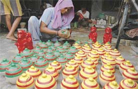 A woman gives a coat of varnish to painted piggy banks and clay idols of Hanuman in Chandan Nagar