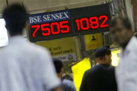 Commuters walk past an electronic board displaying the BSEs index at a railway station in Mumbai
